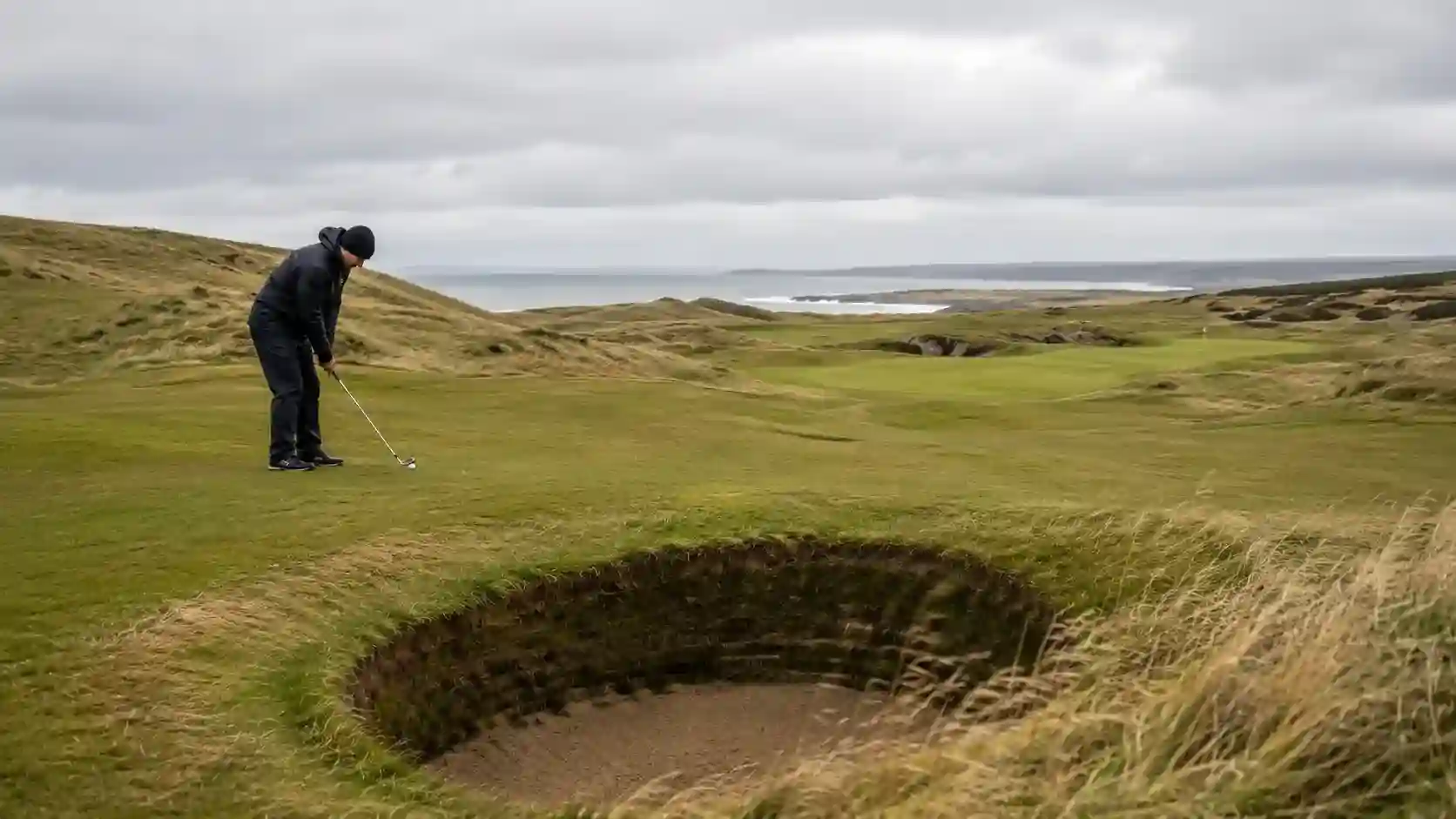 Britischer Links-Golfplatz mit Pot-Bunker und Spieler bei tief stehendem Wind im Vordergrund